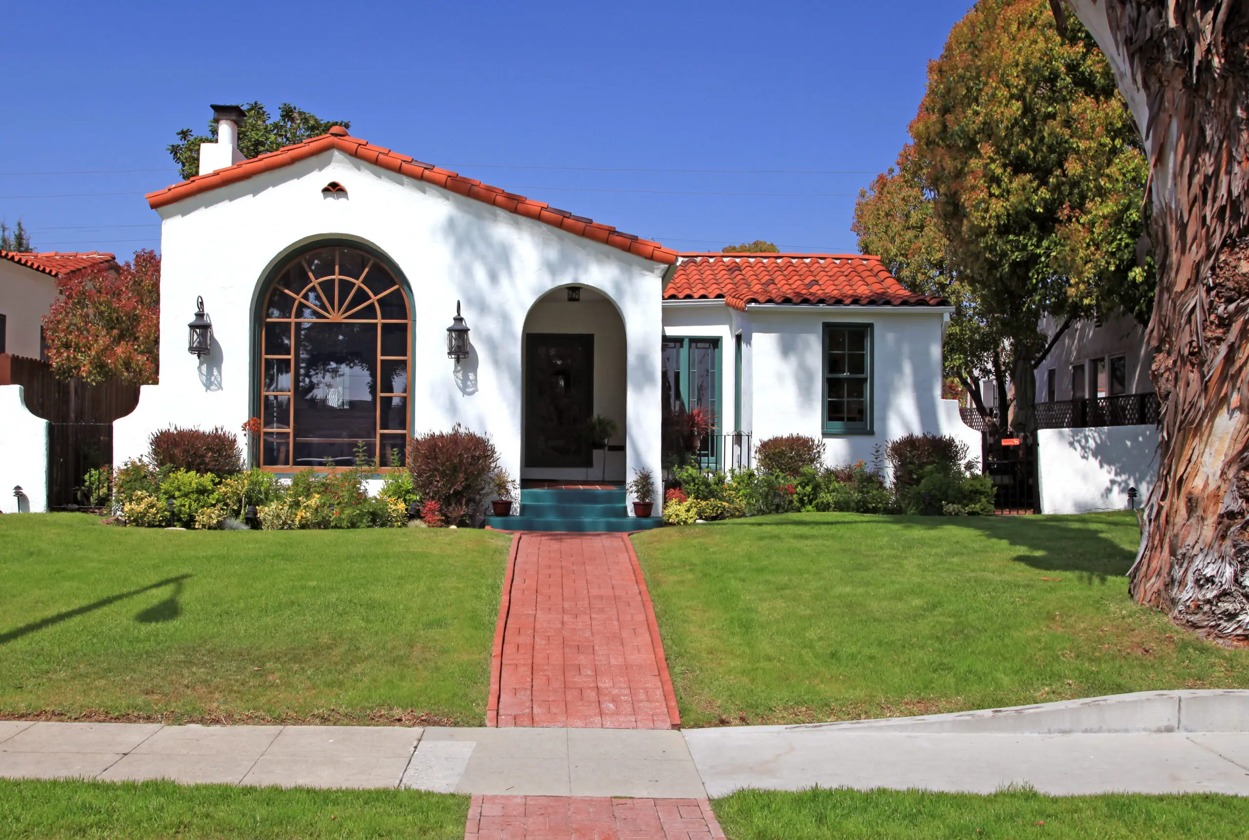 Charming white house with red tile roof and green lawn.
