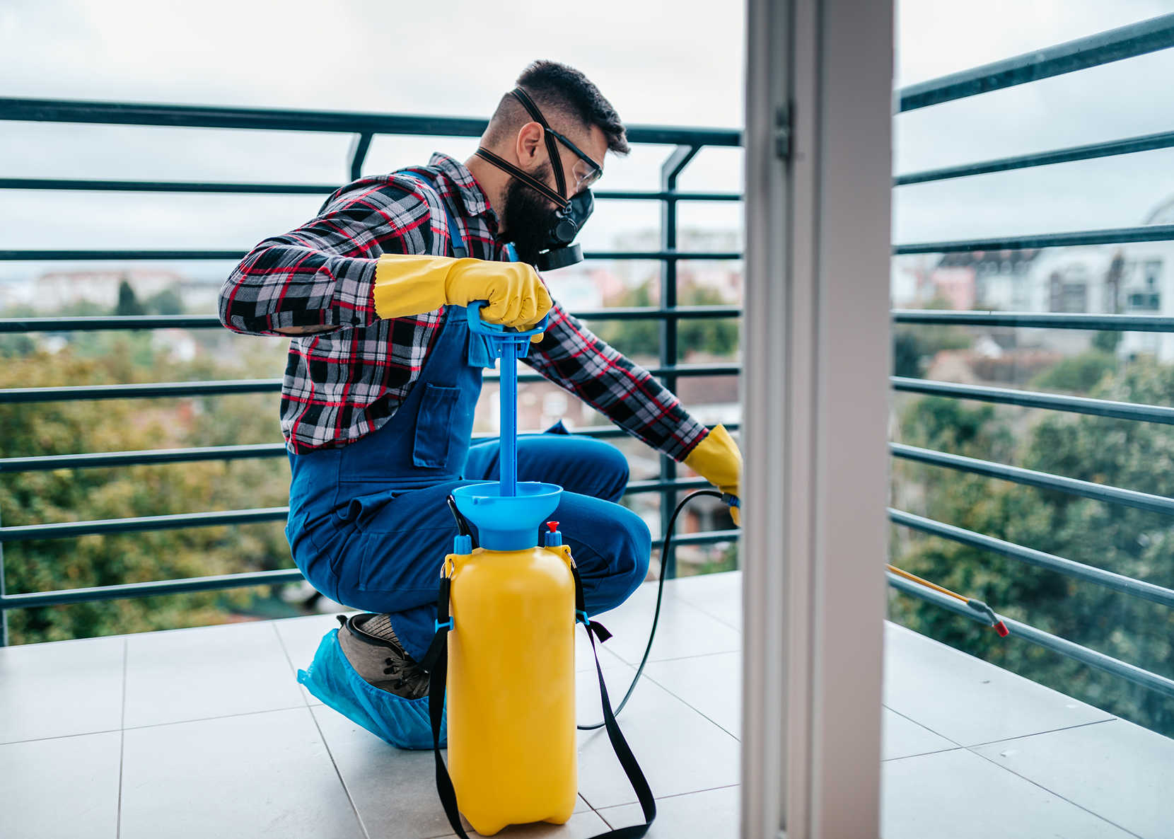 Technician spraying disinfectant on glass door while wearing protective gear.